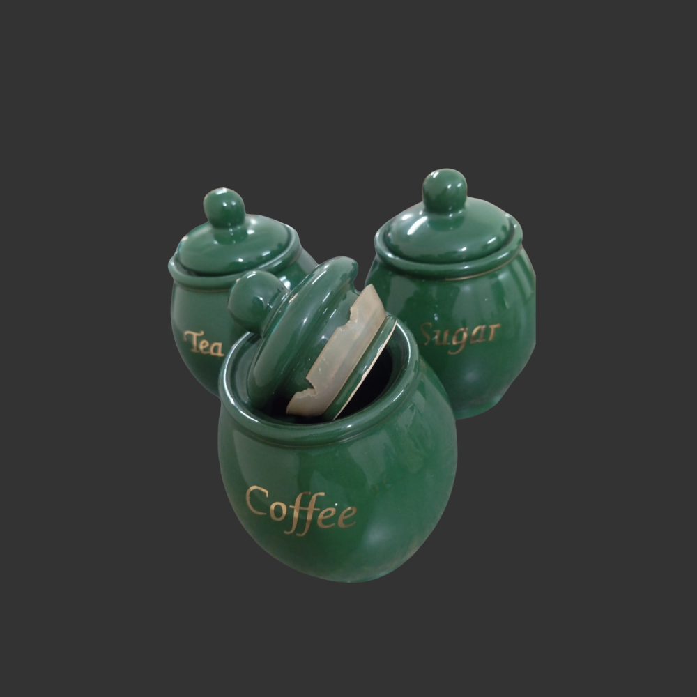 Set of three green ceramic jars labeled 'Tea', 'Coffee', and 'Sugar' on a dark background.