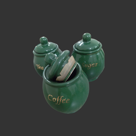 Set of three green ceramic jars labeled 'Tea', 'Coffee', and 'Sugar' on a dark background.
