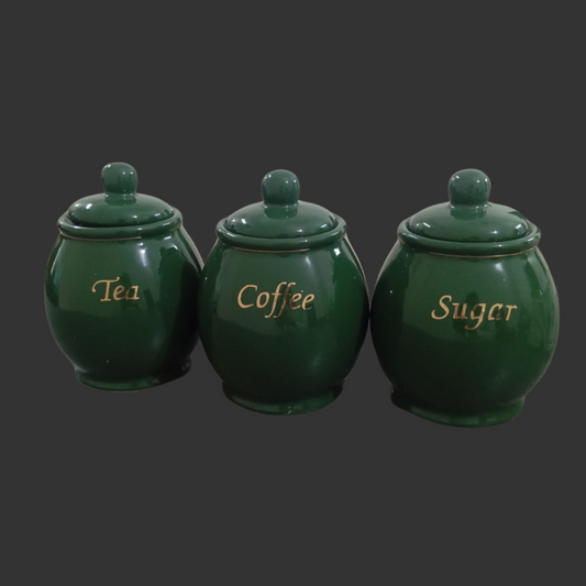 Set of three green ceramic canisters labeled 'Tea', 'Coffee', and 'Sugar' on a dark background.