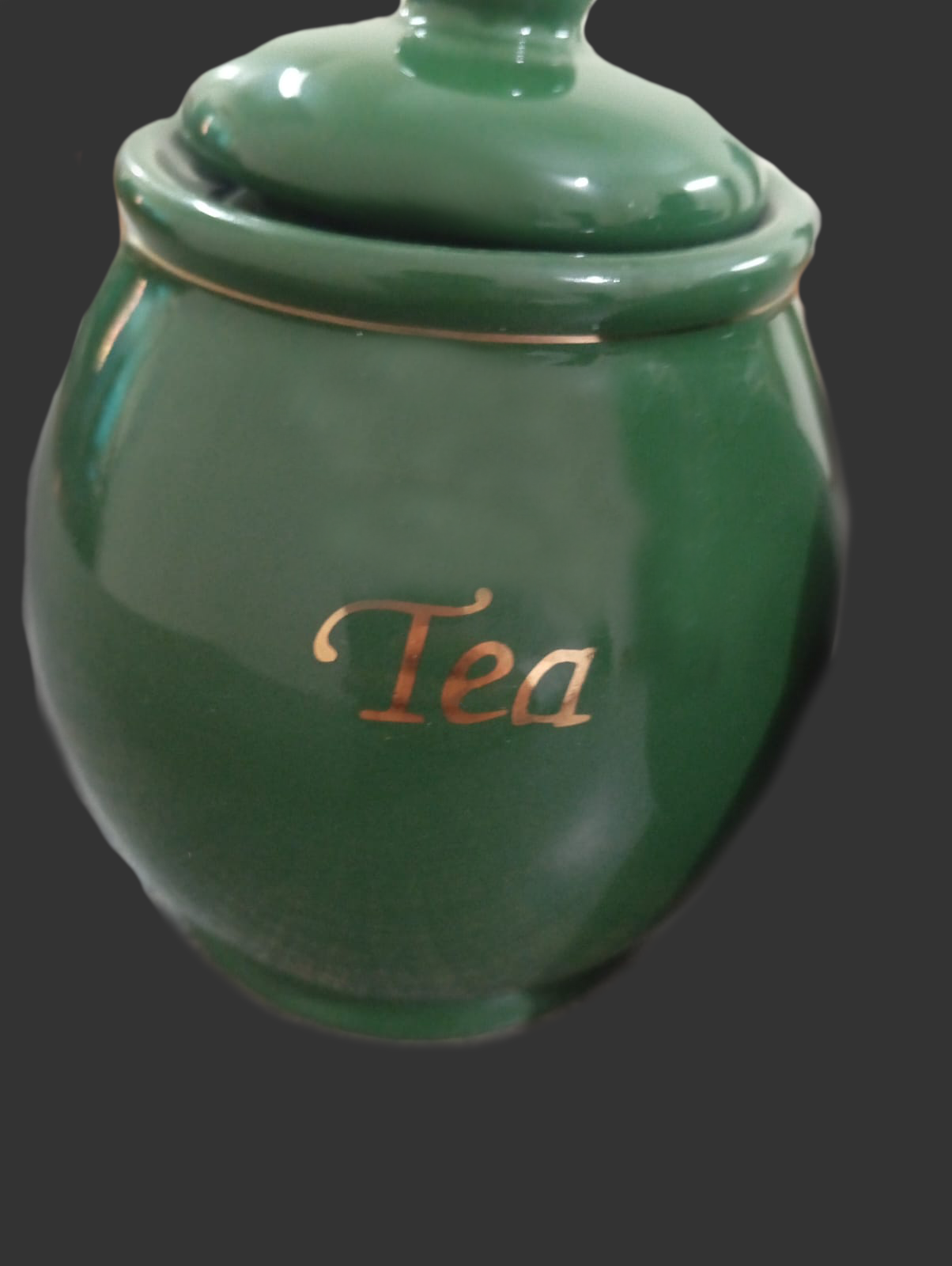 Green ceramic tea jar with 'Tea' inscription on a dark background